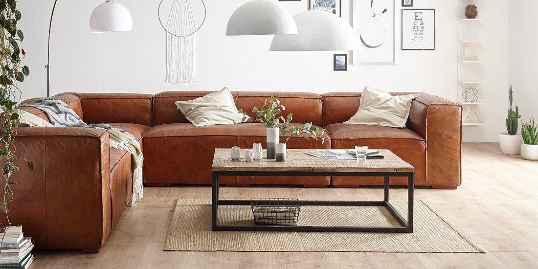 Loft-Wohnzimmer mit industrialen Möbeln: graues Sofa, massiver Holztisch auf Metallgestell, offene Regale, rustikale Atmosphäre