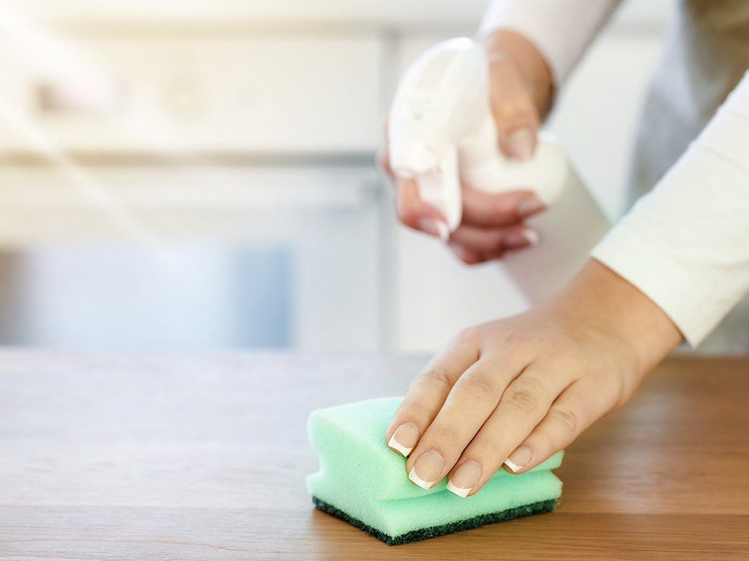 Person wischt mit weichem Tuch Staub von Holzmöbel-Oberfläche – warme Holzfarbe, Nahaufnahme, Möbelpflege