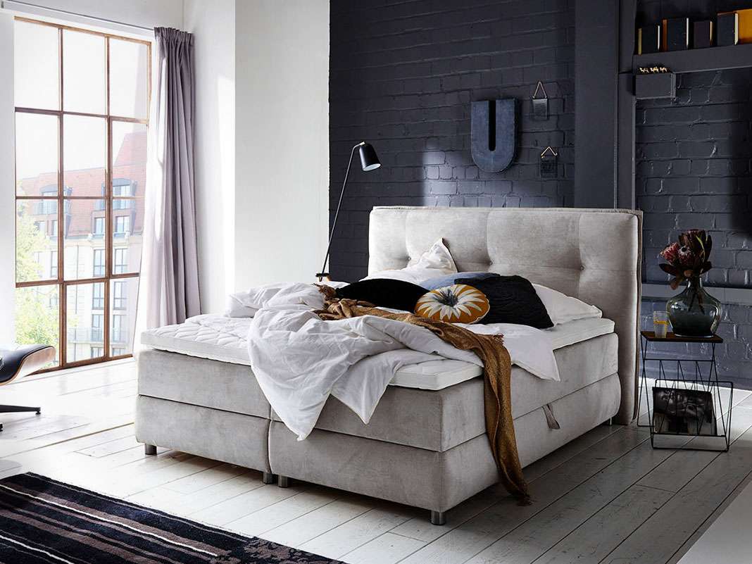Modernes Boxspringbett mit Topper in stilvollem Schlafzimmerambiente, gepolstertes Kopfteil, gemütliche hochwertige Bettwäsche