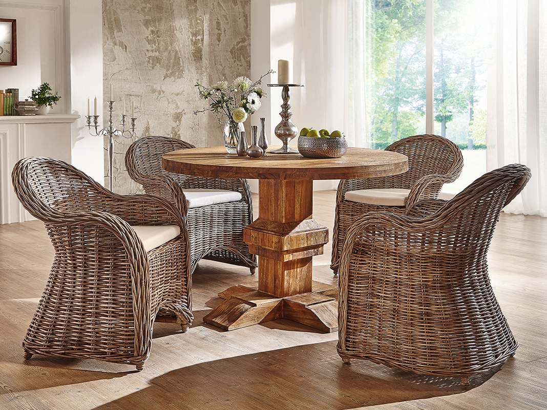 Landhaustisch aus Holz mit Rattanstühlen in gemütlichem Esszimmer, natürliche Farbtöne, rustikales, warmes Ambiente.