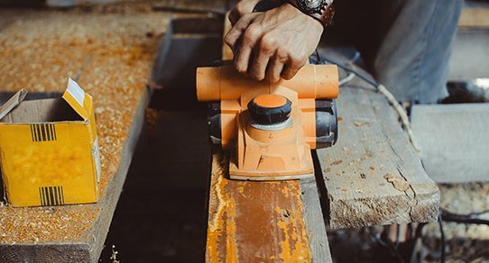 Aufbereitung von recyceltem Holz: gestapelte, aufgearbeitete Bohlen mit Gebrauchsspuren in warmer Werkstatt‑Atmosphäre.