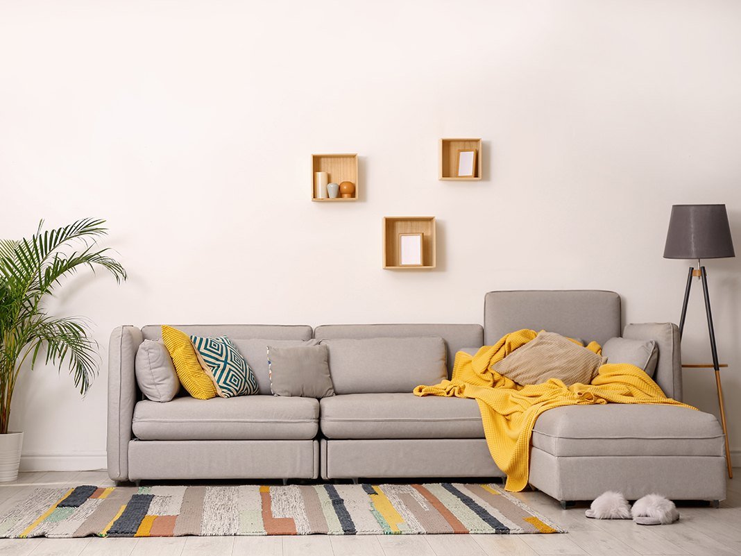 Modernes graues Schlafsofa als Ecksofa in hellem Wohnzimmer mit Stoffbezug, Kissen und Holzfußboden – platzsparende Schlafcouch.